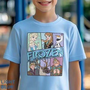 May include: Light blue t-shirt featuring characters from the movie "Frozen." The graphic includes Elsa, Anna, Olaf, Kristoff, Sven, and the text "FROZEN." The shirt is light blue with the words "LIGHT BLUE" printed at the bottom.