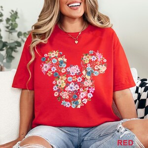 May include: Red t-shirt featuring a floral Mickey Mouse design. The design is composed of various colorful flowers. The word "RED" is printed in the bottom right corner of the image. The shirt is a casual style.