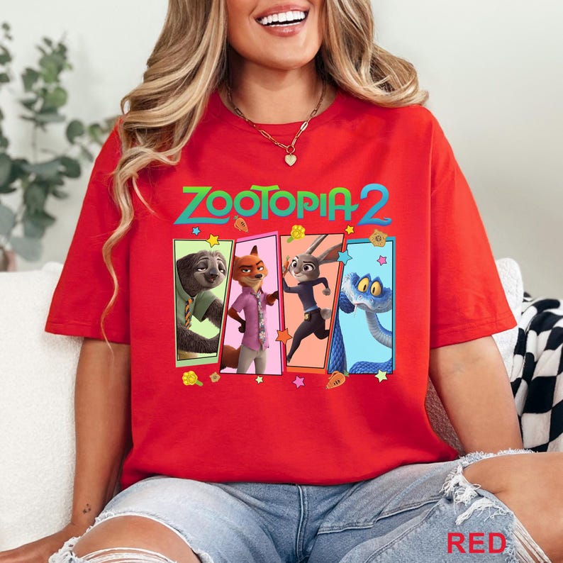 May include: A red t-shirt with the text "ZOOTOPIA 2" in green and a colourful graphic of characters from the film. The graphic includes a sloth, fox, rabbit, and snake. The word "RED" is printed at the bottom.