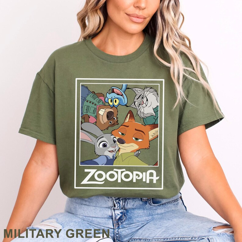 May include: Military green t-shirt with a graphic of characters from the animated film Zootopia. The design includes Judy Hopps, Nick Wilde, and other characters. The word "Zootopia" is printed in white.