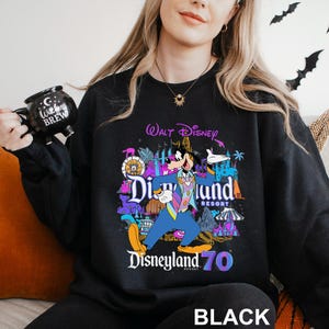 May include: Black sweatshirt featuring a colorful graphic of Goofy in a blue suit, with the words "Disneyland 70 Resort" and "Walt Disney" above. The word "BLACK" is printed at the bottom.
