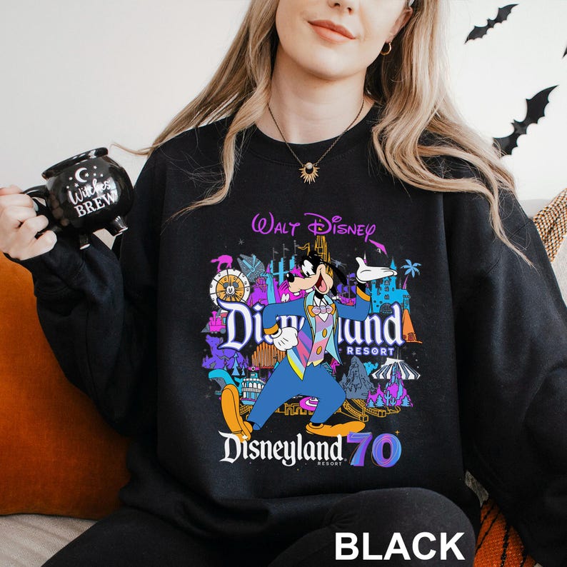 May include: Black sweatshirt featuring a colorful graphic of Goofy in a blue suit, with the words "Disneyland 70 Resort" and "Walt Disney" above. The word "BLACK" is printed at the bottom.