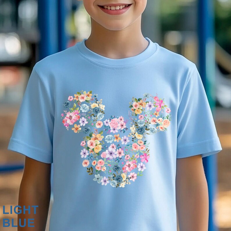 May include: Light blue t-shirt featuring a floral Mickey Mouse design. The design is made up of various colorful flowers, including pink, yellow, and blue. The text "LIGHT BLUE" is printed at the bottom left of the shirt.