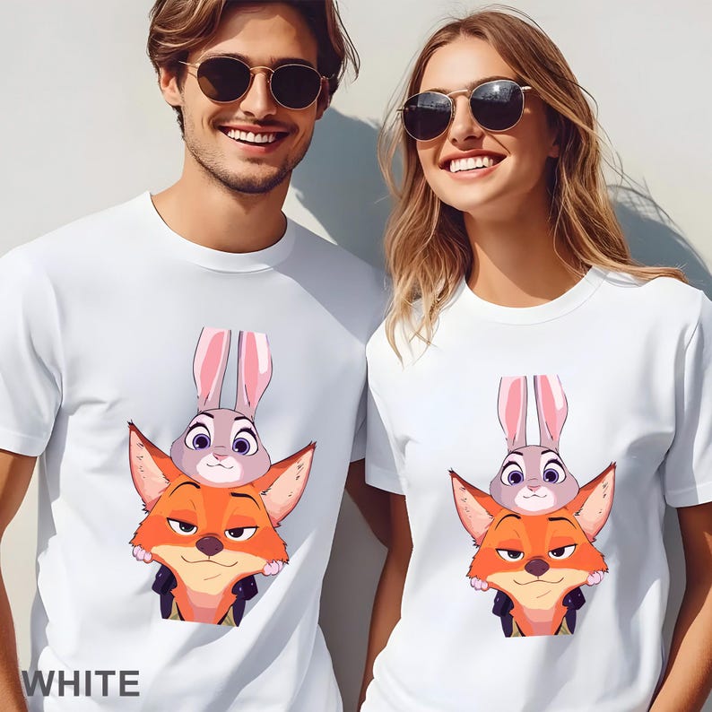 May include: White t-shirts featuring a cartoon fox and bunny design. The fox is orange and the bunny is gray with pink ears. The word "WHITE" is printed at the bottom of the shirt. The shirts are worn by two people.