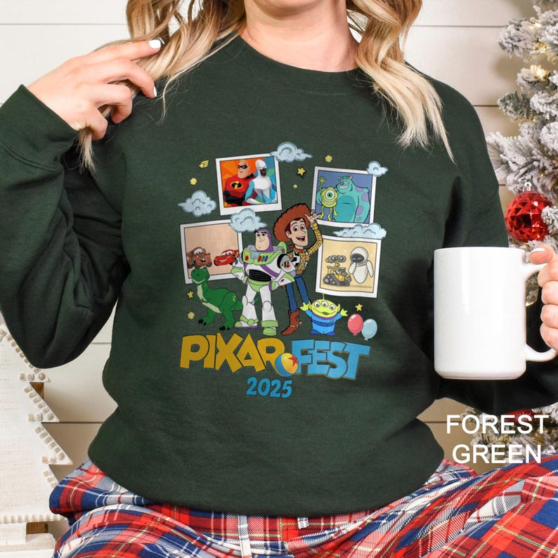Może przedstawiać: Leśna zielona bluza z kolorową grafiką postaci z film&oacute;w Pixara, takich jak Toy Story, Potwory i Sp&oacute;łka i Wall-E. Projekt zawiera napis "PIXAR FEST 2025".