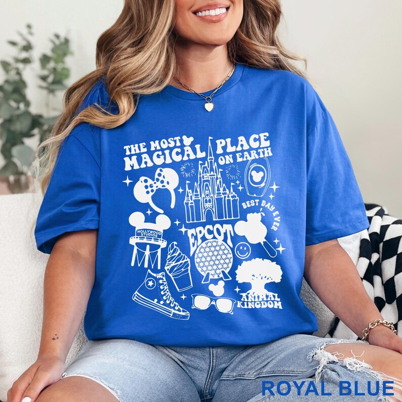 May include: Royal blue t-shirt with a white graphic design featuring the text "The Most Magical Place on Earth" and various Disney-themed icons. The shirt includes images of a castle, Mickey Mouse ears, and other park-related elements.