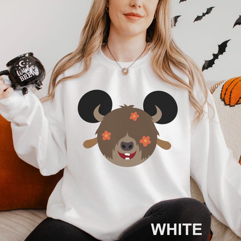 May include: White sweatshirt featuring a cartoon ram design with black ears, brown fur, and orange flowers. The ram has a smiling face with two white teeth. The word "WHITE" is printed at the bottom of the sweatshirt.