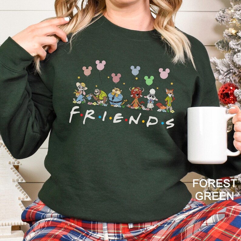 May include: Forest green sweatshirt with the word "FRIENDS" in white, featuring cartoon characters and Mickey Mouse-shaped balloons. The sweatshirt is paired with plaid pants and a white mug.