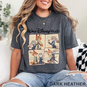 May include: Dark heather gray t-shirt featuring a cartoon graphic of Nick Wilde and Judy Hopps from Zootopia. The graphic includes the text "Walt Disney World" and four panels with different scenes of the characters. The text "Dark Heather" is at the bottom.