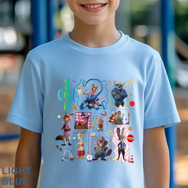 May include: Light blue t-shirt featuring a colorful graphic of characters from the animated movie "Zootopia." The design includes various animal characters and the movie's title. The shirt also has the words "LIGHT BLUE" printed on it.