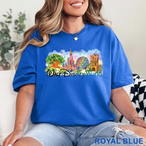 May include: A royal blue t-shirt featuring a colorful graphic print of the Walt Disney World theme park landmarks, including a castle, a geodesic sphere, and a tree, with the text Walt Disney World printed in a black script font across the center.