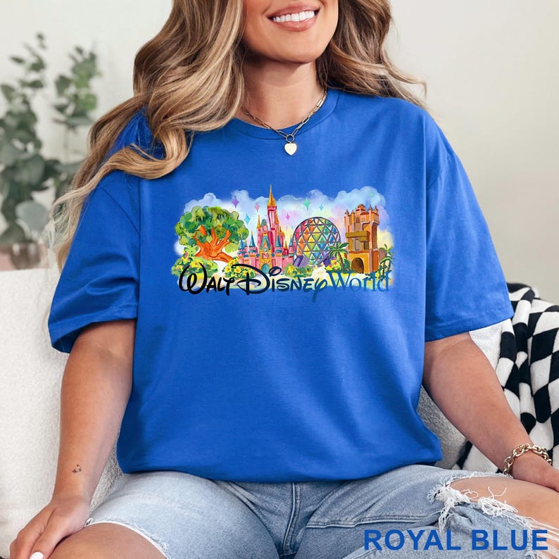 May include: A royal blue t-shirt featuring a colorful graphic print of the Walt Disney World theme park landmarks, including a castle, a geodesic sphere, and a tree, with the text Walt Disney World printed in a black script font across the center.