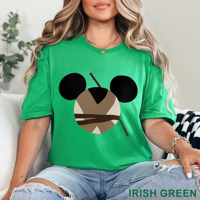 May include: A green t-shirt with a graphic design featuring a stylized face with black ears, a brown and beige center, and two brown lines. The text "IRISH GREEN" is at the bottom of the image.