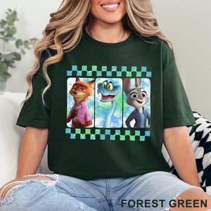 May include: Forest green t-shirt featuring three cartoon characters in a film strip design. The characters include a fox in a pink shirt, a blue snake, and a rabbit in a blue jacket. The shirt is made of a soft material.