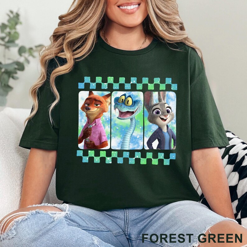 May include: Forest green t-shirt featuring three cartoon characters in a film strip design. The characters include a fox in a pink shirt, a blue snake, and a rabbit in a blue jacket. The shirt is made of a soft material.