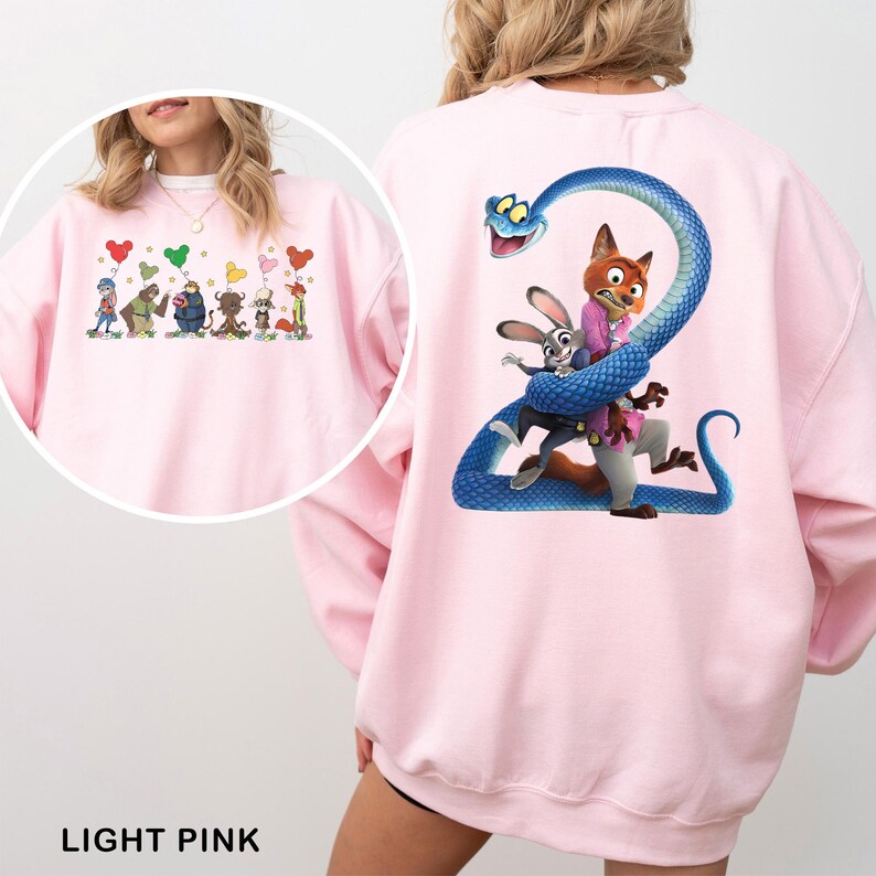 May include: A light pink sweatshirt featuring a large graphic on the back of a blue snake coiled around a fox and a rabbit. A circular inset shows the front of the sweatshirt with a line of small cartoon characters holding Mickey-shaped balloons.