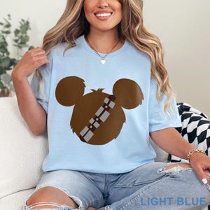 May include: Light blue t-shirt featuring a brown graphic design. The design combines elements of a popular character with Mickey Mouse ears. The text "LIGHT BLUE" is at the bottom of the image.