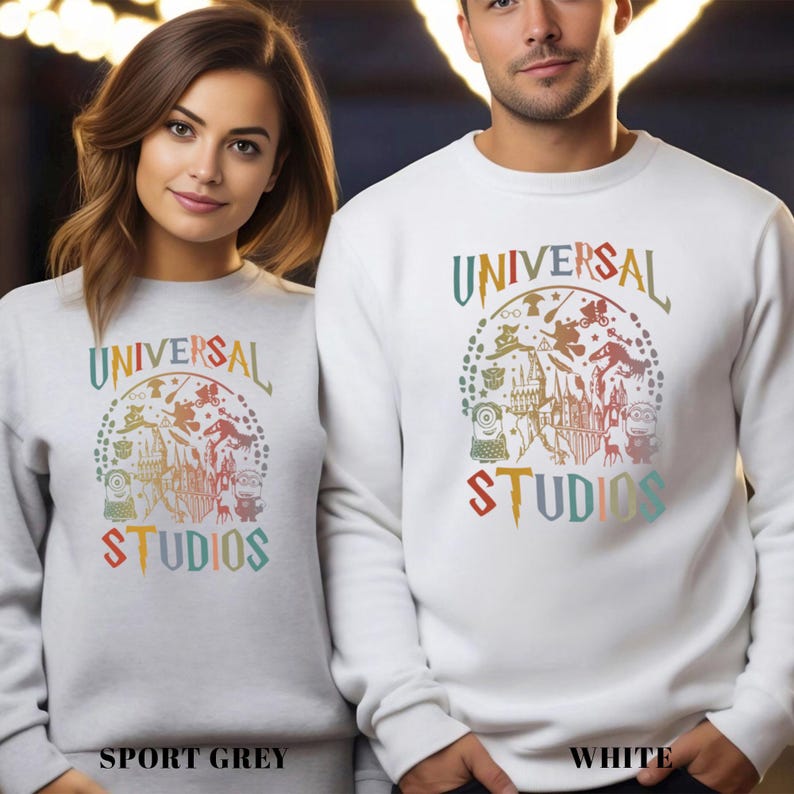 Pode incluir: Camisolas cinza desportivas e brancas com um gr&aacute;fico colorido da Universal Studios. O design inclui o texto "UNIVERSAL STUDIOS" e v&aacute;rios personagens de desenhos animados. As camisolas s&atilde;o de manga comprida.