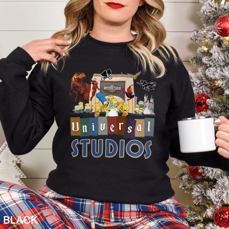 May include: Black crewneck sweatshirt featuring a colorful graphic of Universal Studios characters, including the Simpsons, Minions, and Spider-Man. The words "Universal Studios" are printed in blue and gold. The word "BLACK" is printed at the bottom.