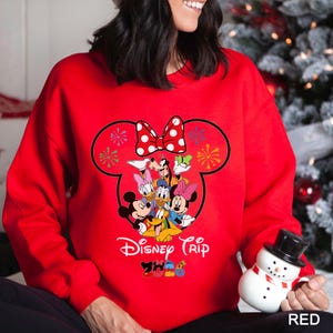 May include: A red sweatshirt featuring a Minnie Mouse head outline with a white polka dot bow. Inside the outline are Mickey, Minnie, Donald, Daisy, and Goofy. The words "Disney Trip" and "2023" are printed below the characters.