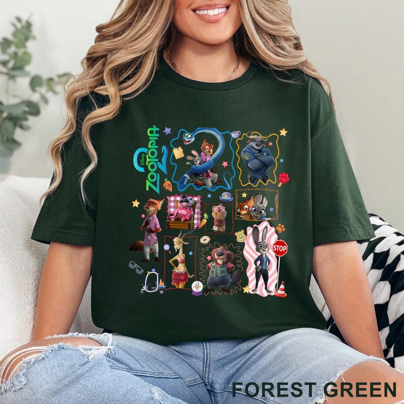 May include: Forest green t-shirt featuring a colorful graphic of characters from the animated movie Zootopia. The design includes various animal characters in a collage-style arrangement, with the word "Zootopia" in green. The shirt is made of a soft material.