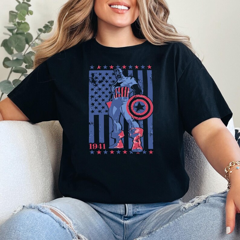 May include: Black t-shirt featuring a patriotic graphic of a superhero with a shield, set against a backdrop of the American flag. The design includes the year "1941" and stars. The shirt is a classic crew neck.