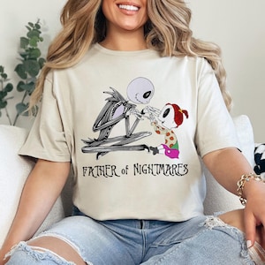 Puede incluir: Camiseta beige con una ilustraci&oacute;n en blanco y negro de Jack Skellington y un ni&ntilde;o. El texto "FATHER OF NIGHTMARES" est&aacute; impreso debajo. El dise&ntilde;o est&aacute; inspirado en Pesadilla antes de Navidad.
