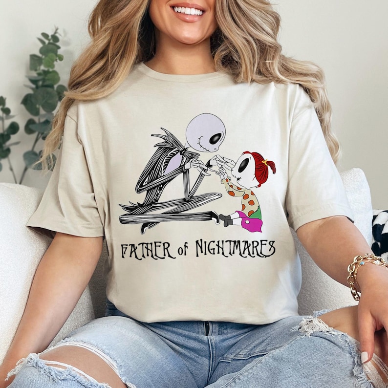 Puede incluir: Camiseta beige con una ilustraci&oacute;n en blanco y negro de Jack Skellington y un ni&ntilde;o. El texto "FATHER OF NIGHTMARES" est&aacute; impreso debajo. El dise&ntilde;o est&aacute; inspirado en Pesadilla antes de Navidad.