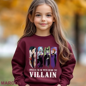 Puede incluir: Una sudadera burdeos con un estampado de cuatro villanos de dibujos animados y el texto "Sweetie I'm OK with being the Villain". La sudadera es de cuello redondo.