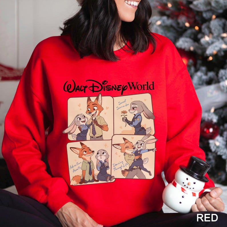 May include: A red sweatshirt featuring a Walt Disney World logo and a four-panel cartoon design. The cartoon depicts characters from Zootopia in various poses, with text including "Adventure Awaits" and "Dancing Through Life."
