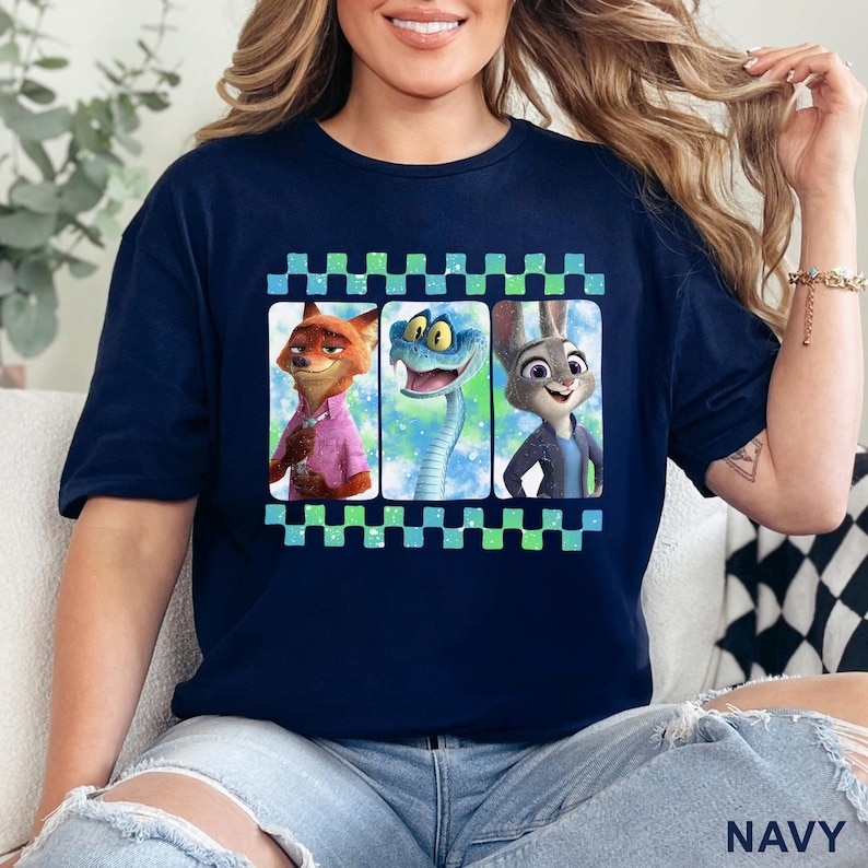 May include: Navy blue t-shirt featuring three characters from Zootopia: Nick Wilde, a snake, and Judy Hopps. The characters are in a checkered frame. The word "NAVY" is printed at the bottom of the shirt.