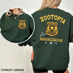May include: Forest green sweatshirt featuring the Zootopia Police Department logo on the front and back. The back design includes the word "Zootopia" above the badge, and "Police Department" below, with three stars.