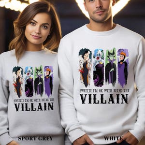 Puede incluir: Sudaderas deportivas grises y blancas con un gr&aacute;fico de cuatro villanos de dibujos animados. El texto "SWEETIE I'M OK WITH BEING THE VILLAIN" est&aacute; impreso debajo de los personajes. Las sudaderas se muestran en una persona.