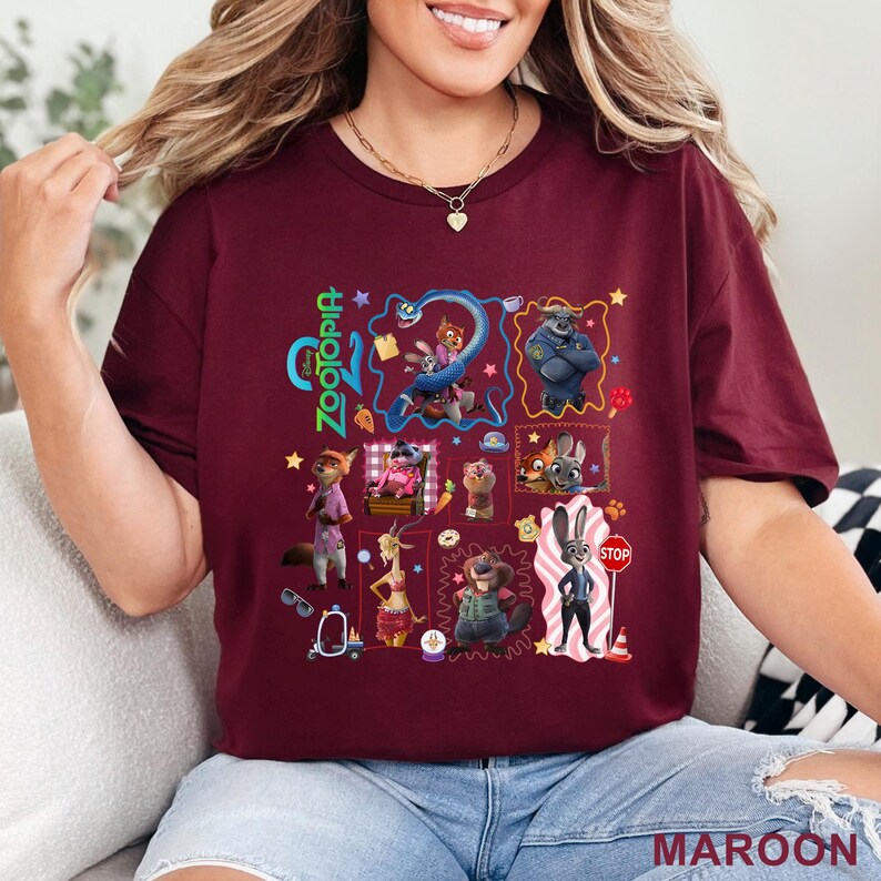 May include: Maroon t-shirt featuring a colorful graphic of characters from the animated film Zootopia. The design includes the film's title and various animal characters in a collage-style arrangement. The shirt is made of a soft material.