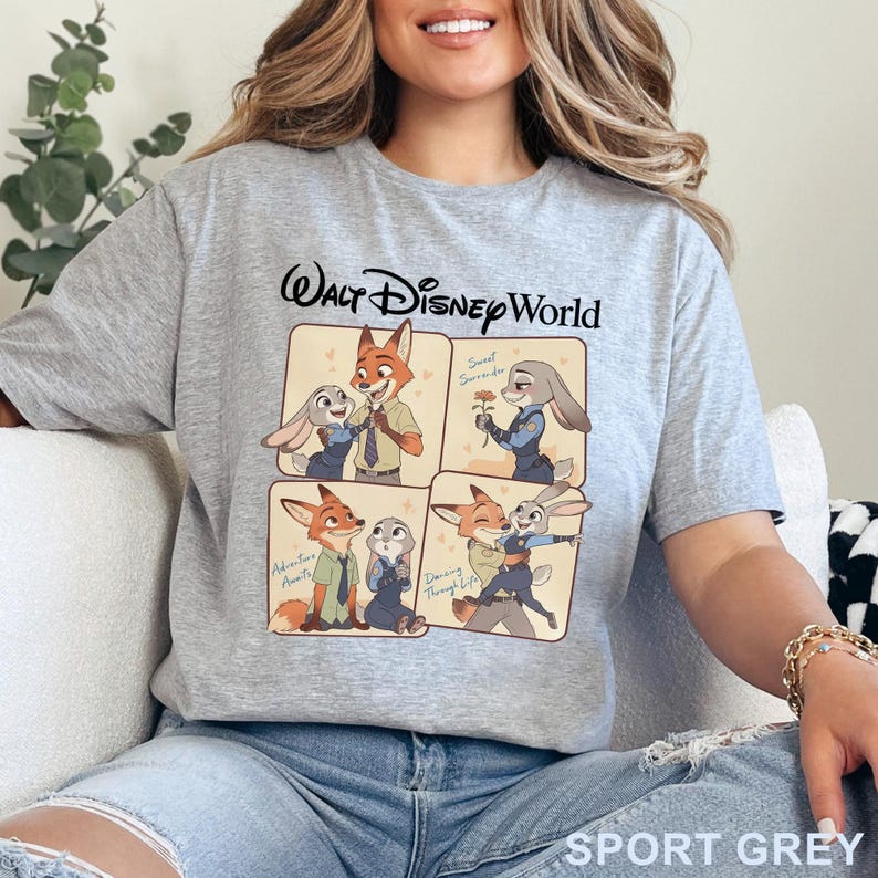 May include: Sport grey t-shirt featuring a cartoon graphic of Nick Wilde and Judy Hopps from Zootopia. The shirt has the words "Walt Disney World" printed at the top. The graphic shows the characters in four different scenes. The words "Adventure Awaits", "Sweet Surrender", and "Dancing Through Life" are also printed on the shirt.