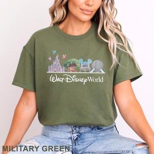 Op de afbeelding: Een olijfgroen t-shirt met korte mouwen en een afbeelding van de Walt Disney World skyline, inclusief het kasteel, de boom, het studio-bord en de geodetische bol, met de tekst Walt Disney World in het wit onder de afgebeelde bezienswaardigheden.