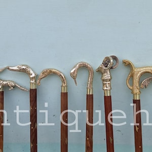 May include: A selection of decorative walking sticks with animal-shaped handles. The handles are made of brass and feature designs including a bird, a fox, a duck, and a ram. The sticks have dark brown wooden shafts.