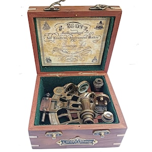 May include: A vintage nautical instrument set in a wooden case. The case is open, revealing brass instruments, including a sextant and magnifying glasses, set against a green velvet lining. The case has brass hardware and the text "J. Scott London 1753".