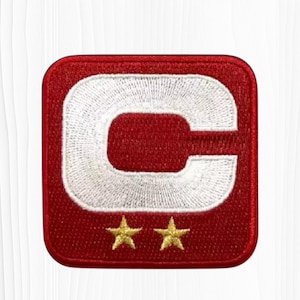 May include: Embroidered patch featuring a large white letter "C" on a red background. Two gold stars are positioned below the letter. The patch has a square shape with rounded corners, suitable for apparel or accessories.