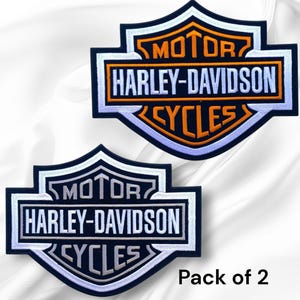 May include: Two Harley-Davidson Cycles embroidered patches. Each patch features the Harley-Davidson logo in white, orange, and black. The patches are in a shield shape with the words "MOTOR", "HARLEY-DAVIDSON", and "CYCLES". The text "Pack of 2" is in the bottom right corner.
