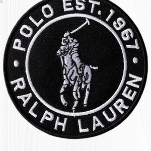 May include: Black and white embroidered patch featuring the Polo Ralph Lauren logo. The circular patch has the words "POLO EST. 1967. RALPH LAUREN" embroidered around the edge. The central image is a polo player on a horse.
