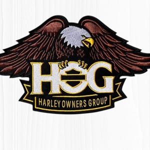 May include: Embroidered patch featuring a brown and black eagle with outstretched wings. The eagle is above the white and gold letters "HOG" and the words "HARLEY OWNERS GROUP" on a black banner.