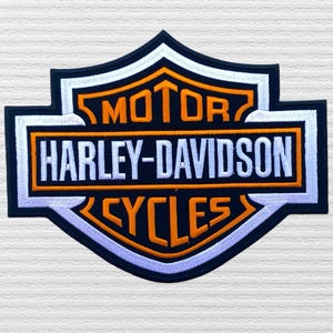 May include: Embroidered Harley-Davidson patch featuring the brand's logo in orange and white on a navy blue shield shape. The text "MOTOR HARLEY-DAVIDSON CYCLES" is prominently displayed.