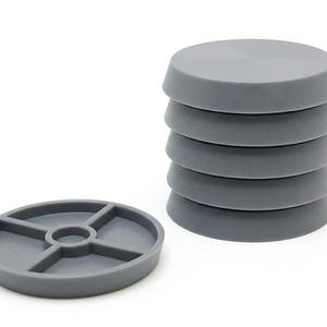 Pode incluir: Uma pilha de cinco bases circulares de plástico cinzento para móveis com uma superfície superior lisa, acompanhada por uma base colocada na horizontal para revelar a parte inferior, com um anel central e quatro suportes radiais.
