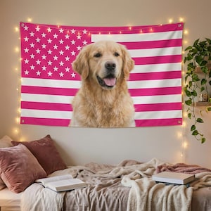 May include: A tapestry featuring a golden retriever dog with a pink and white American flag design. The dog is centered, with its tongue out. The flag has pink stripes and white stars. The tapestry is hanging above a bed.