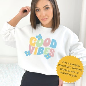 K&ouml;nnte beinhalten: Wei&szlig;er Pullover mit einem bunten "GOOD VIBES"-Motiv und blauen Blumenakzenten. Dies ist ein digitaler Download, es wird nichts physisches verschickt.