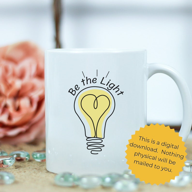 May include: White ceramic mug with a black outline of a light bulb with a yellow heart inside. The text "Be the Light" is written around the light bulb.