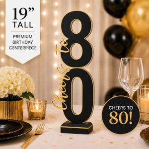 May include: A 19-inch tall black and gold birthday centerpiece featuring the number 80 and the text Cheers to 80. The design includes a vertical black number 80 with gold trim, a gold script Cheers to, and a circular black sign with gold text.