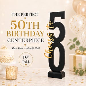 May include: A matte black number 50 centerpiece standing 19 inches tall, featuring the gold script text Cheers to 50. The text on the image reads THE PERFECT 50TH BIRTHDAY CENTERPIECE, Matte Black + Metallic Gold, and 19 INCH TALL.