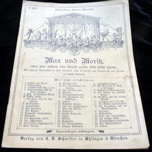 Könnte beinhalten: Ein vergilbtes Papiercover für ein Kindertheaterstück mit dem Titel „Max und Moritz“. Das Cover zeigt eine Illustration einer Bühne mit Figuren und Text auf Deutsch. Das Cover stammt vom Verlag J.F. Schreiber.